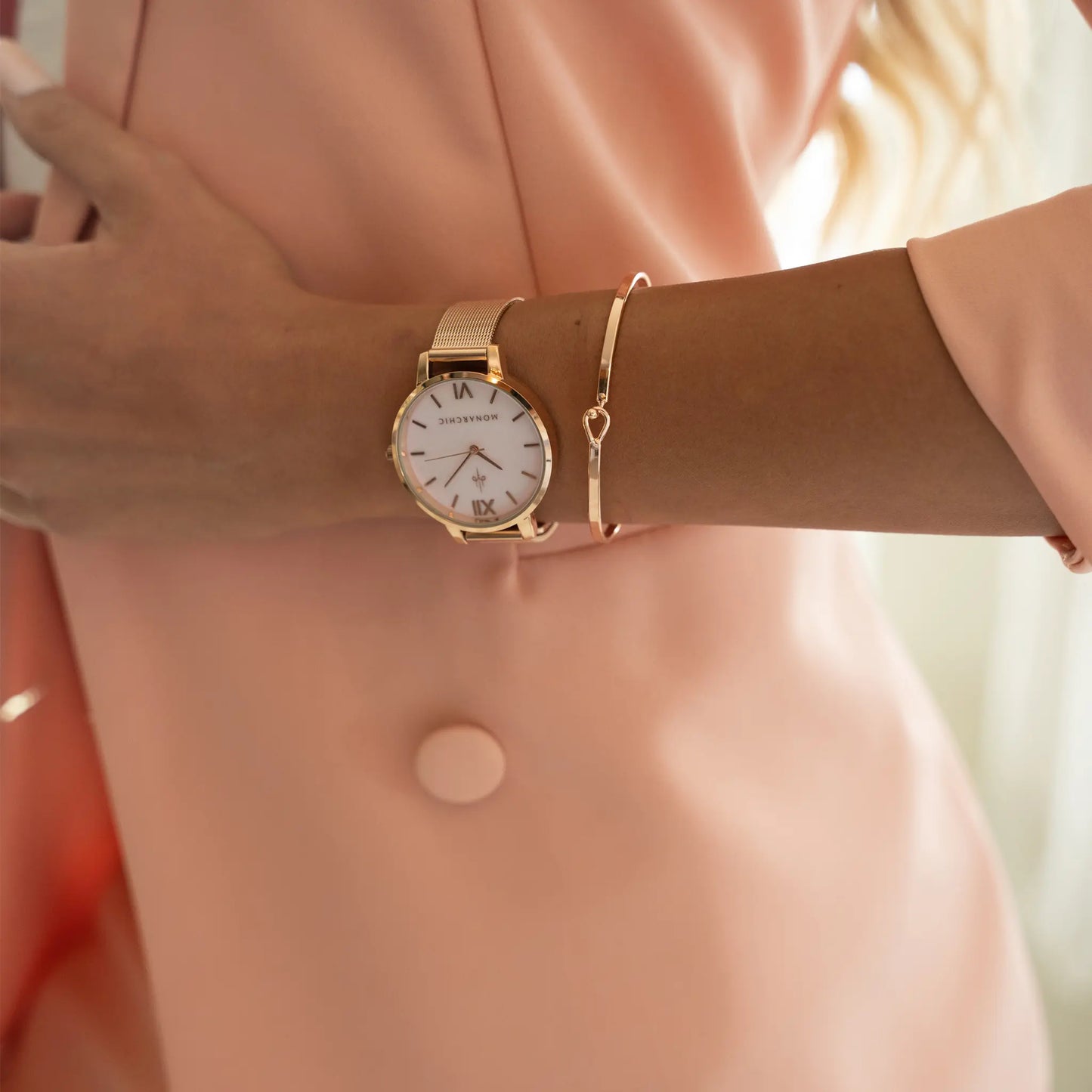 Wrist view of the Monarchic® Kelly Rose Gold watch styled with a peach blazer and rose gold bracelet.