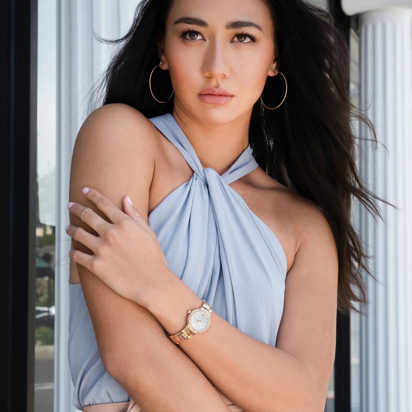 Model wearing Monarchic® Watch - Cosmopolitan - Jackie Edition - Gold link watch with large hoop earrings and soft blue jumpsuit